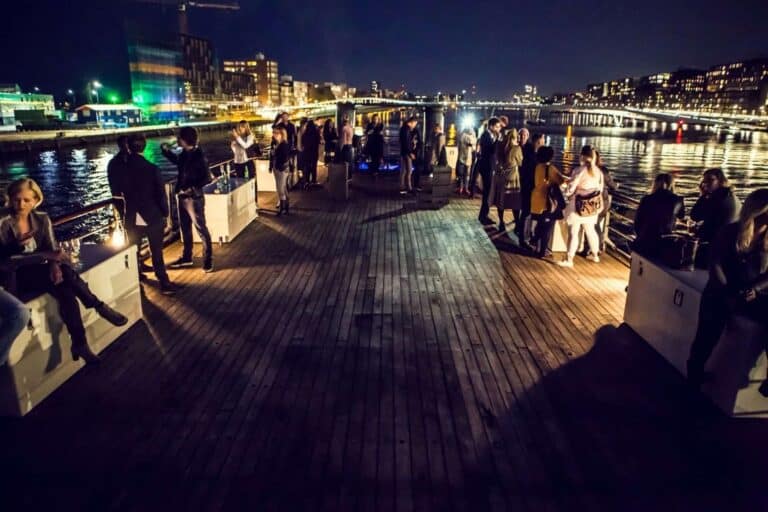 Partychater op het water bij nacht met gasten en skyline op de achtergrond.